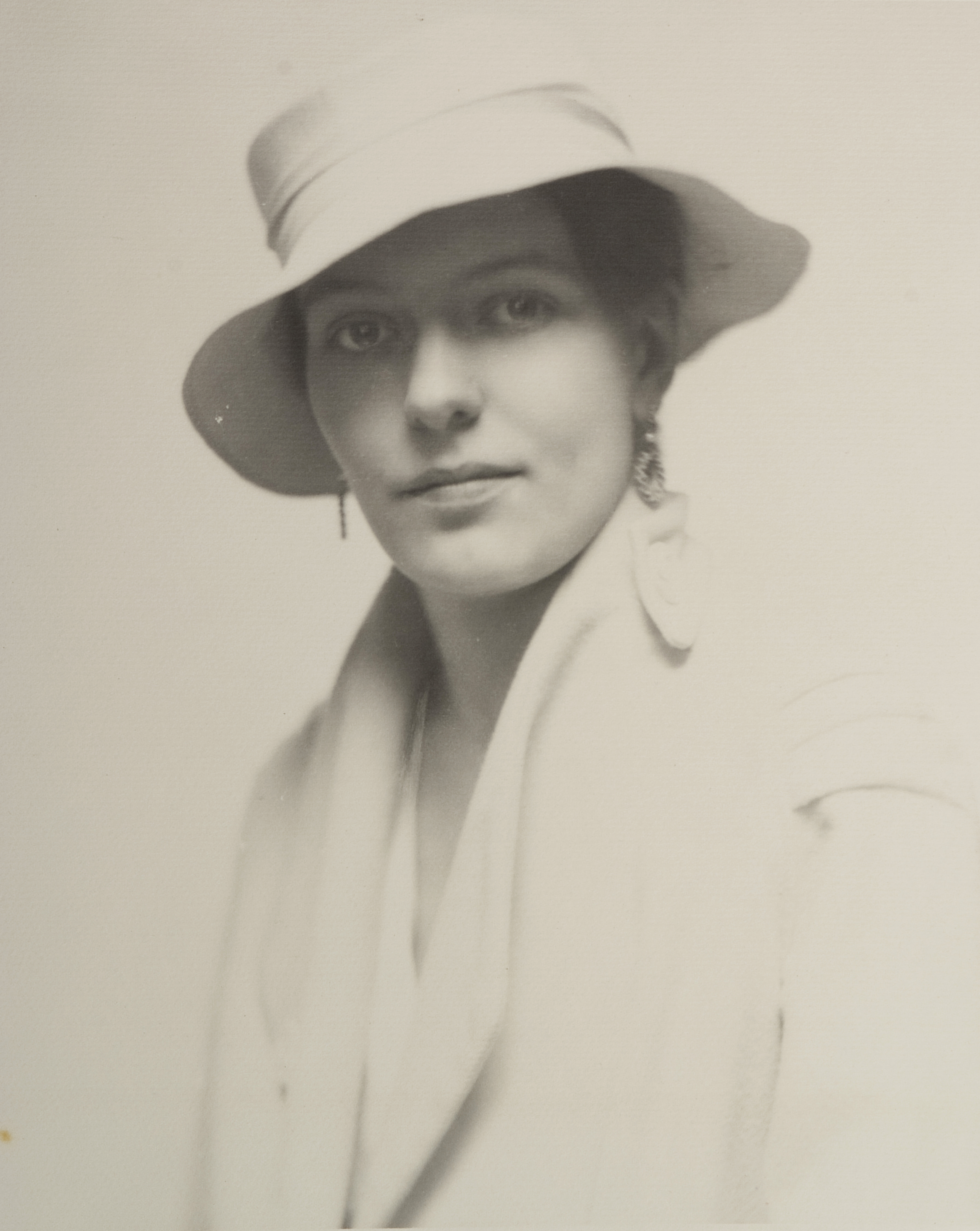 Portrait of woman wearing earrings, white hat, white coat, looking at camera