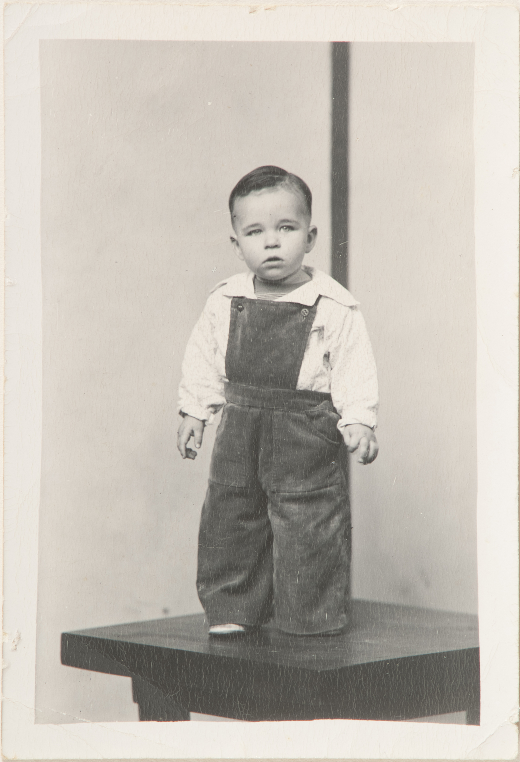 Boy on table in white shirt and rompers, striped background