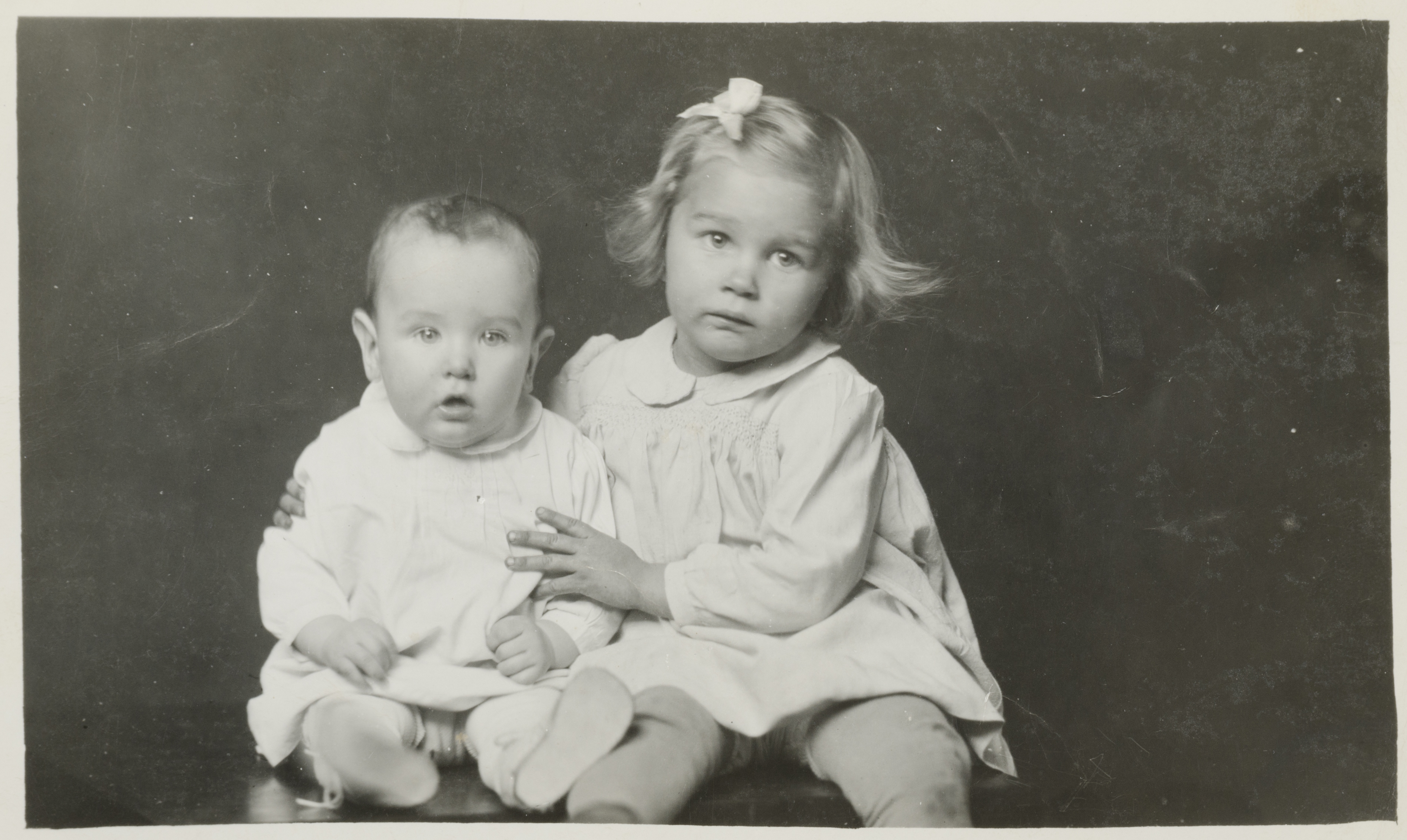 Little girl with arms around baby sibling, both seated