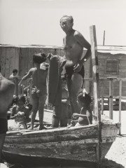 Man standing, children seated in boat, all in bathing suits