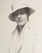 Portrait of woman wearing earrings, white hat, white coat, looking at camera
