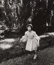 Girl in hat and white printed dress, running through woods