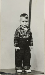 Little boy in plaid shirt, pants with suspenders, striped background