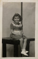 Untitled [Smiling young girl seated on table, striped background]